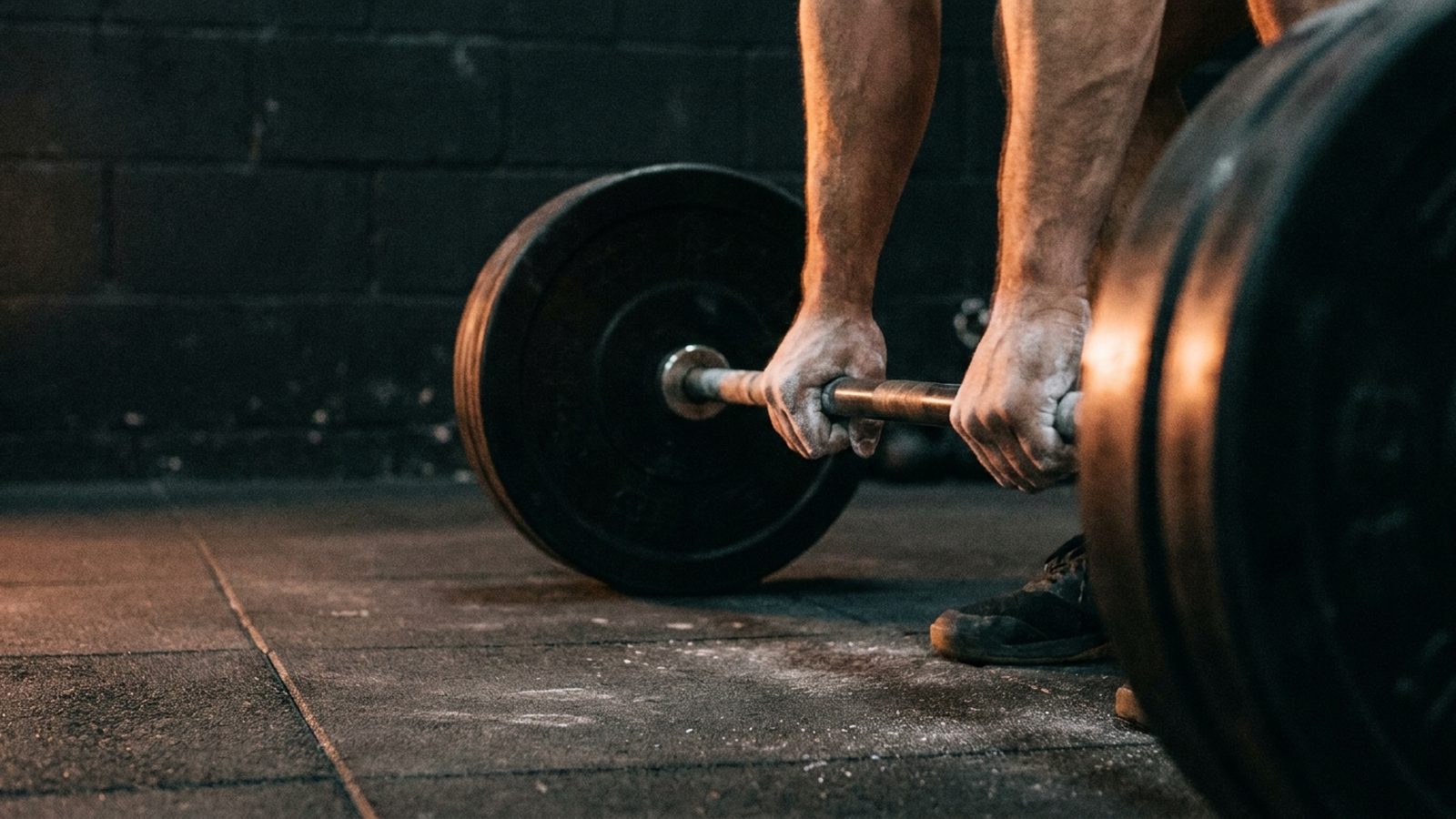 A man's chalked hands gripping a loaded barbell mid-deadlift, gripping through a rep he doesn't feel like doing
